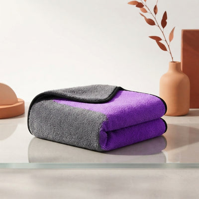 A premium dual-sided plush car cleaning cloth neatly folded on a reflective surface against a clean white and terracotta back